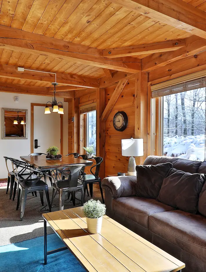 Living room of a vacation-rental cabin in Killington, VT. Snow and trees outside seen through two large windows.