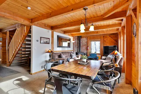 View of the living room of The Cabin at Killington. Wooden features, cozy sofas, mirror on the wall and large dinner table.